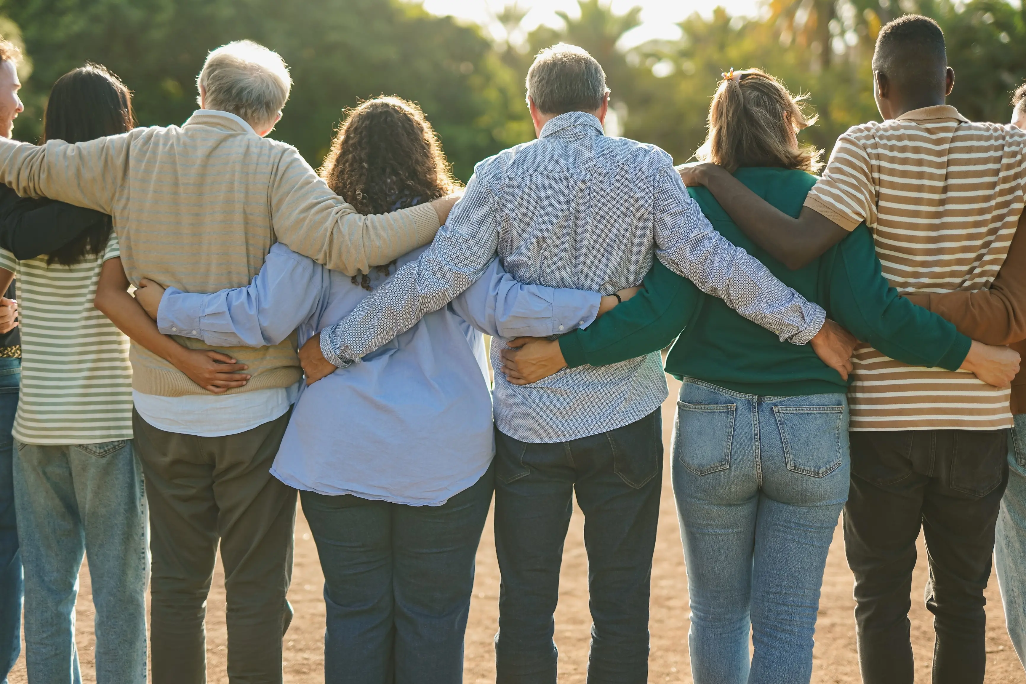 <p>Group of multiracial people hugging each other at city park - Back view of multi generational community outdoor</p>\\n